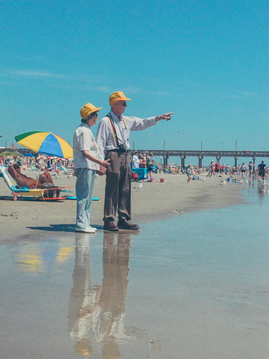 Un couple âgé sur une plage aux couleurs rétro, lui montre l’horizon
