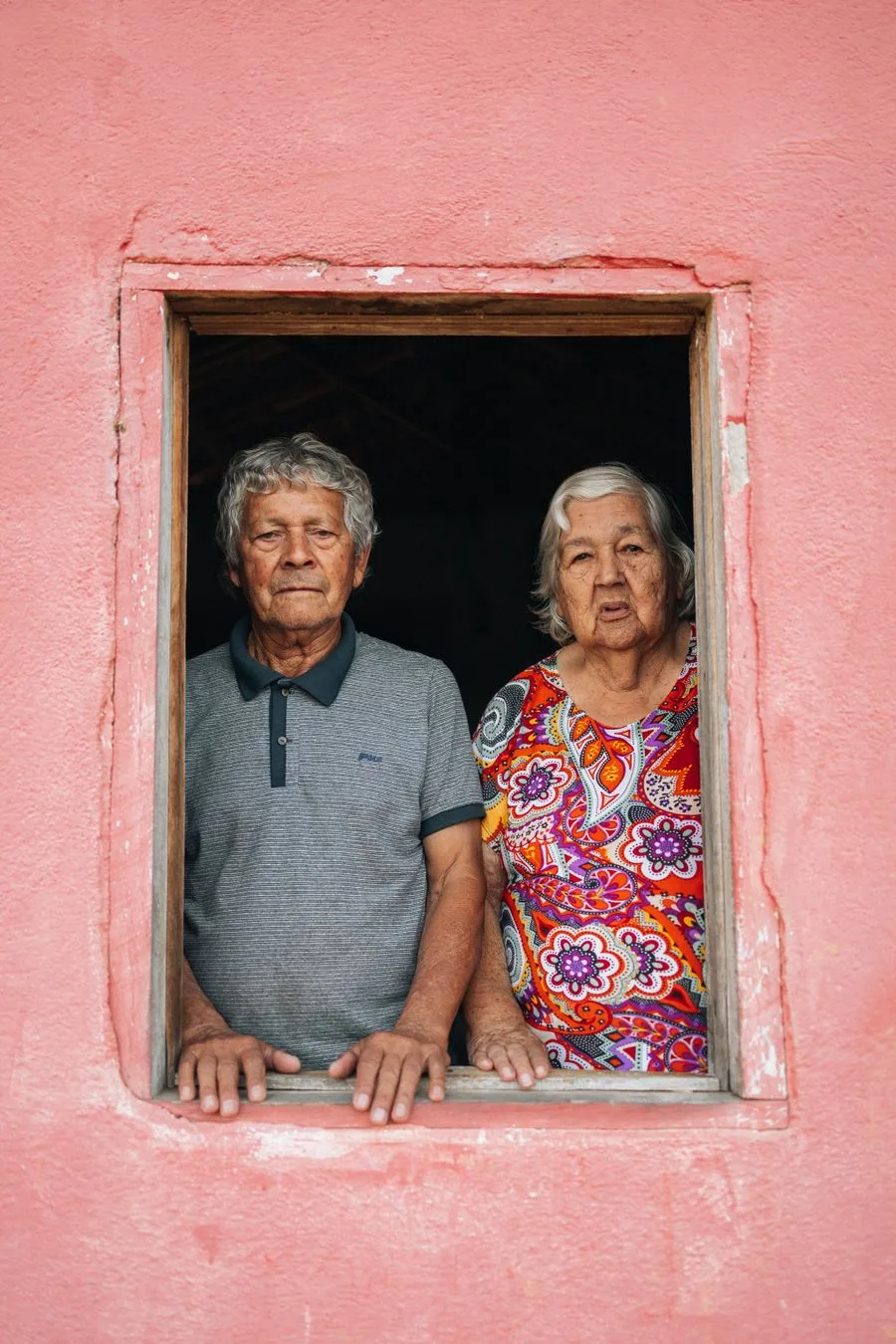Un couple de grands-parents à la fenêtre d’une maison au mur rose